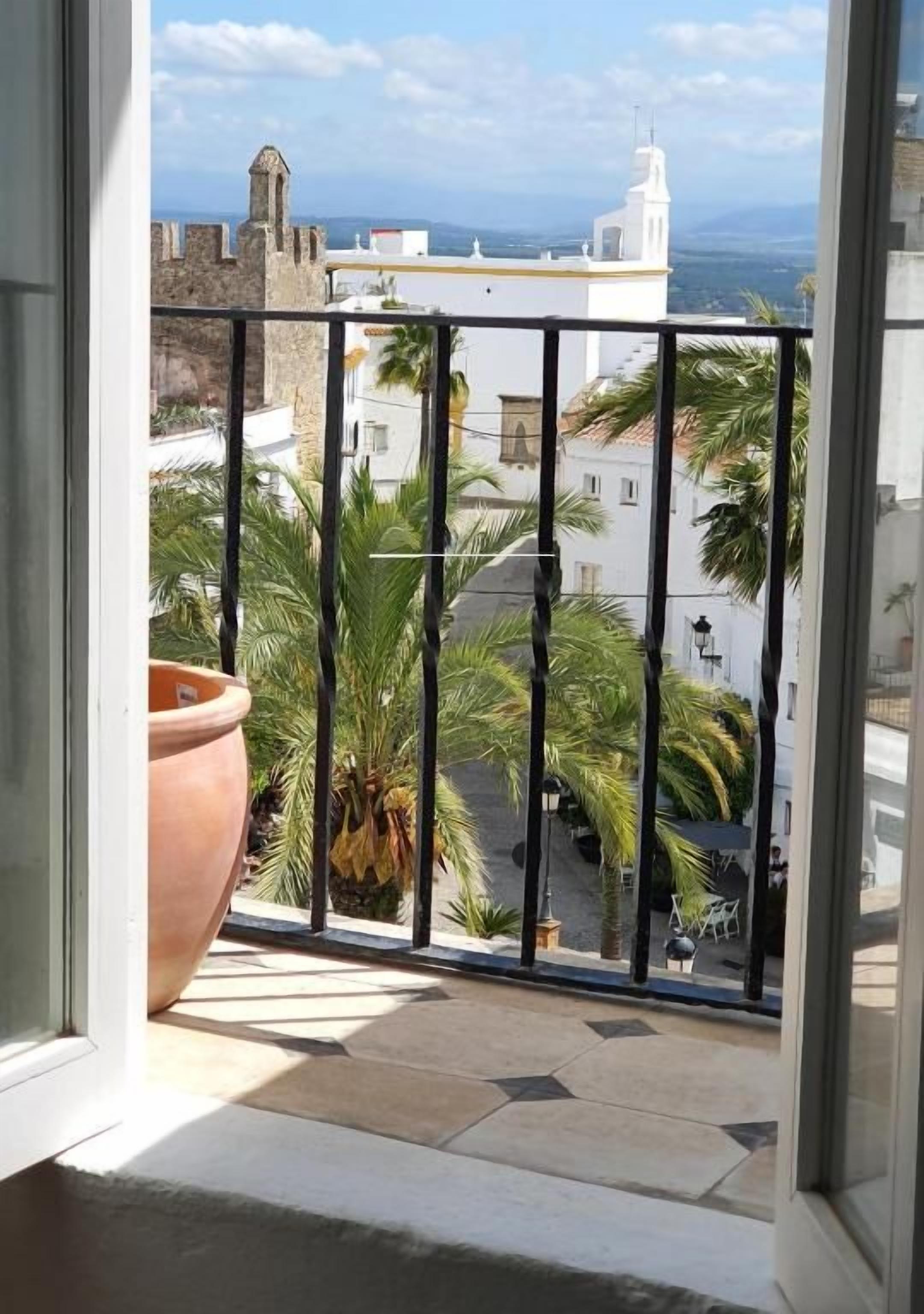 Un balcon offrant une vue sur un bâtiment historique, des palmiers et un ciel dégagé.