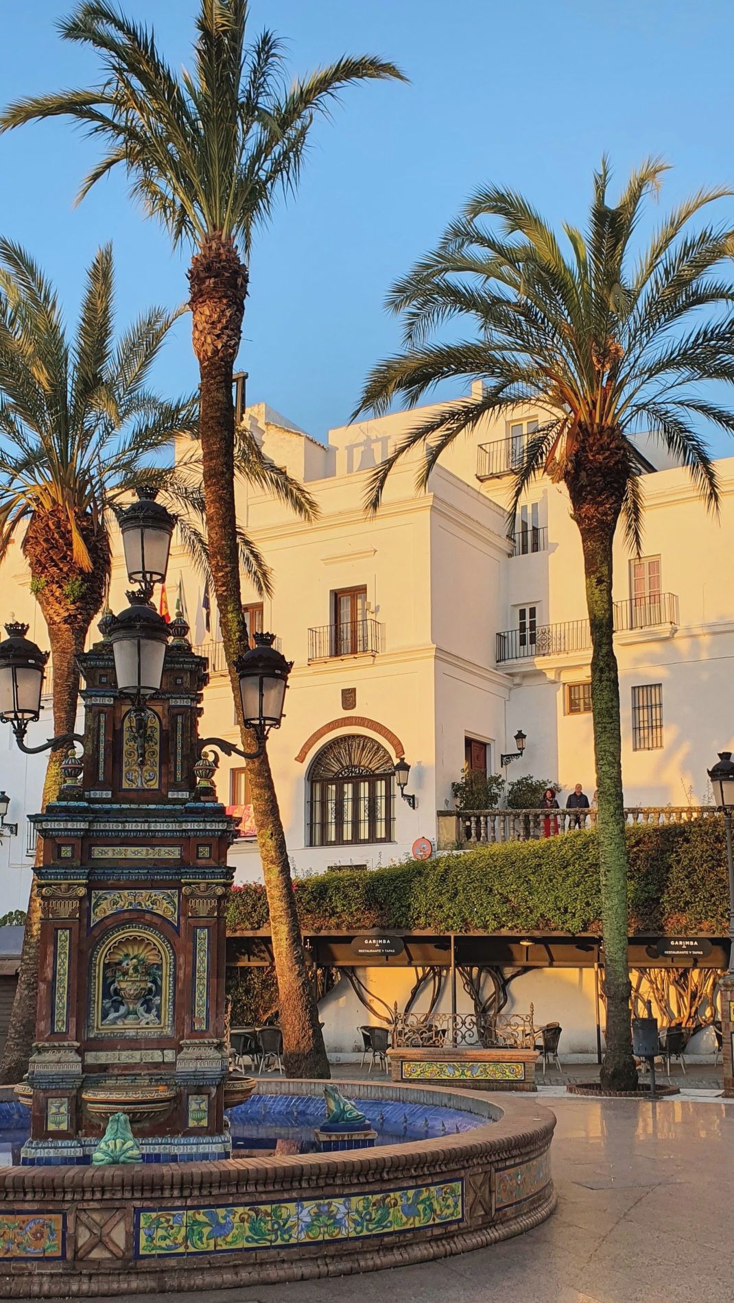 Una plaza con una fuente, palmeras y un edificio con balcones.