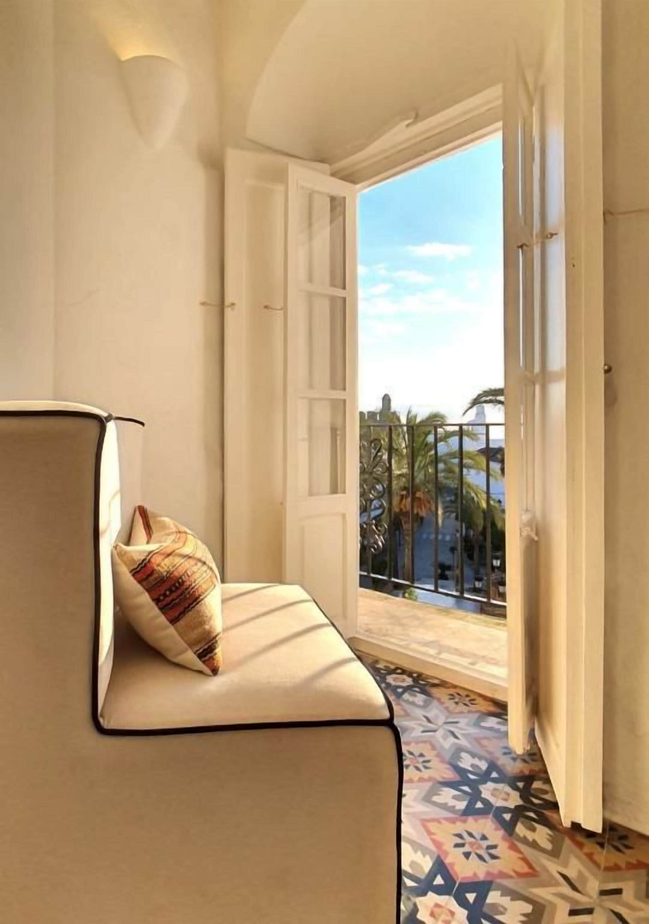 Ein Zimmer mit einer Couch, einem gemusterten Kissen, einem gemusterten Boden und Blick durch eine Tür nach draußen.