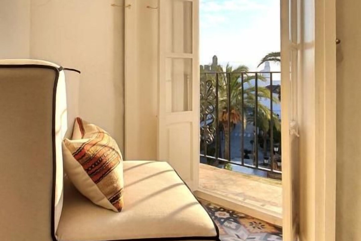 A room with a sofa, a patterned pillow, a patterned floor, and a view through a door to the outside.