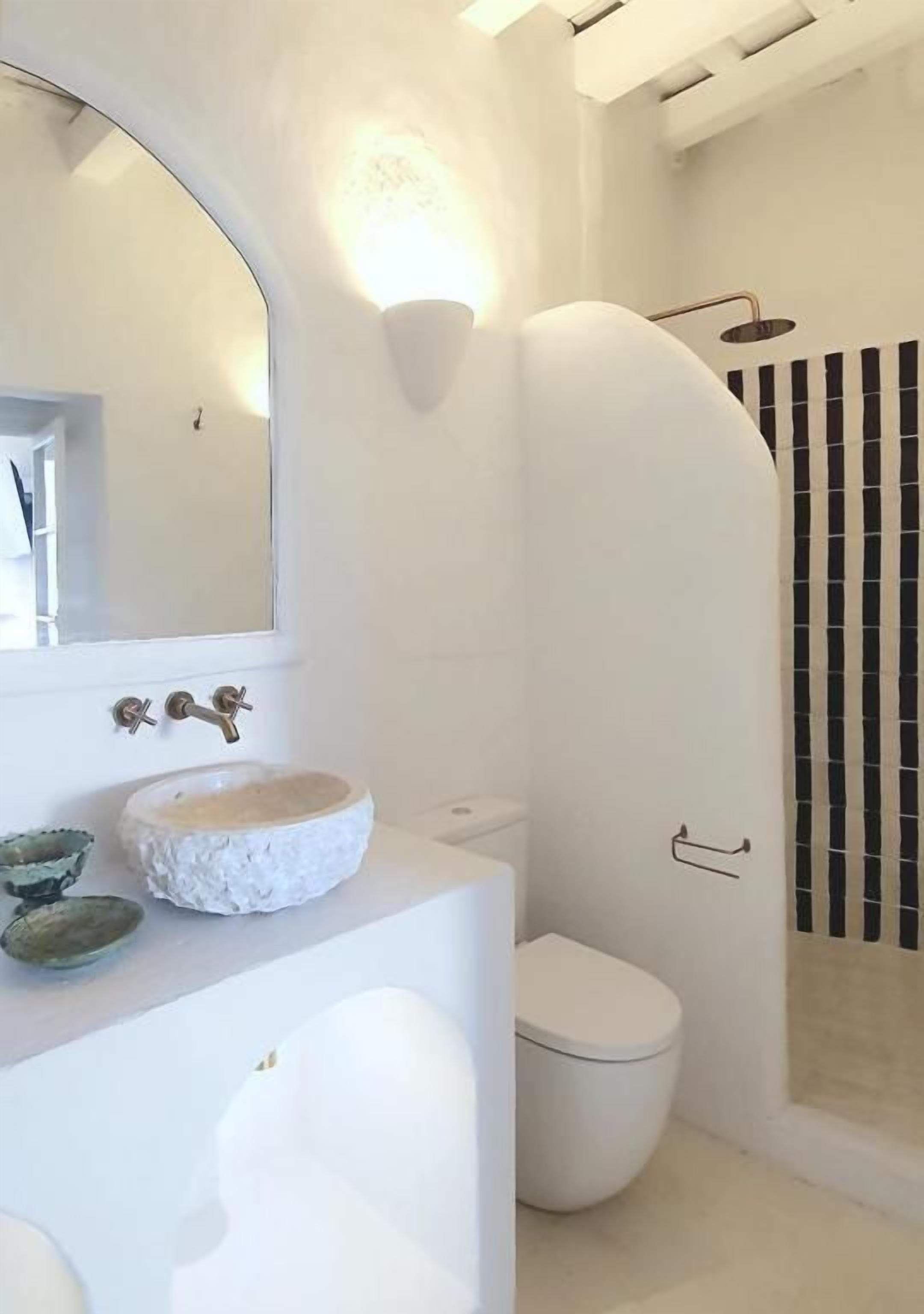 A bathroom with a white sink, a round mirror, a toilet, and a shower area.