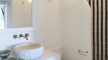 A bathroom with a white sink, a round mirror, a toilet, and a shower area.