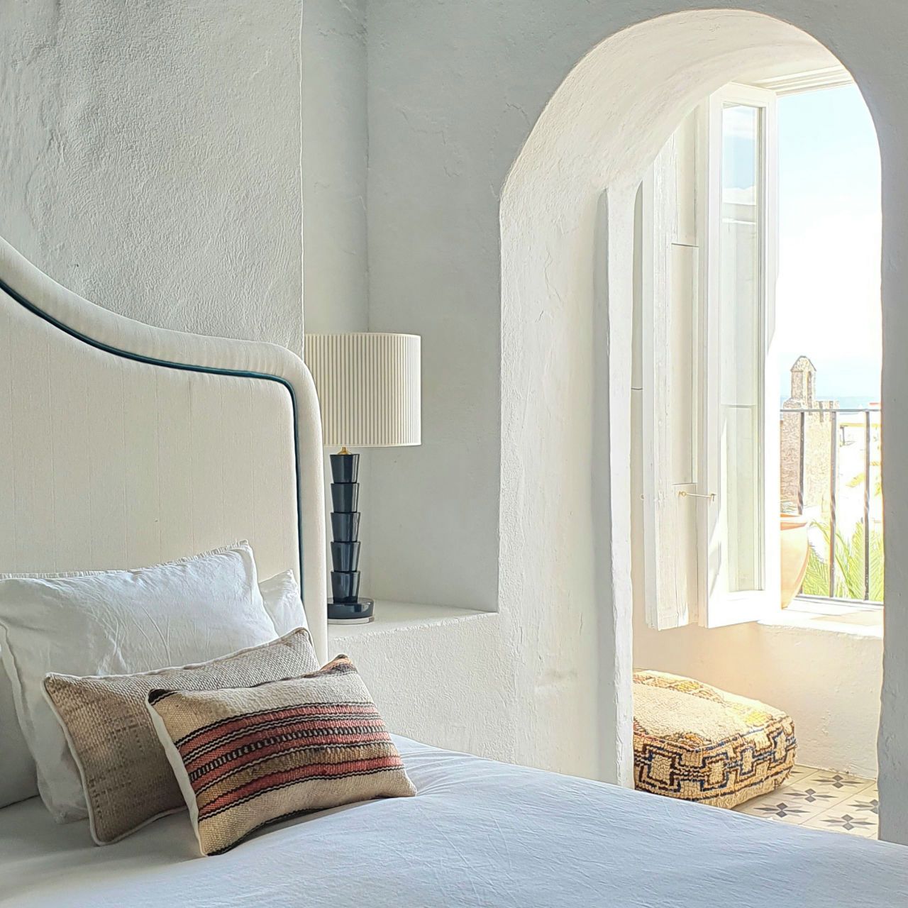 Un dormitorio con cama, almohadas, una lámpara y vistas al exterior.