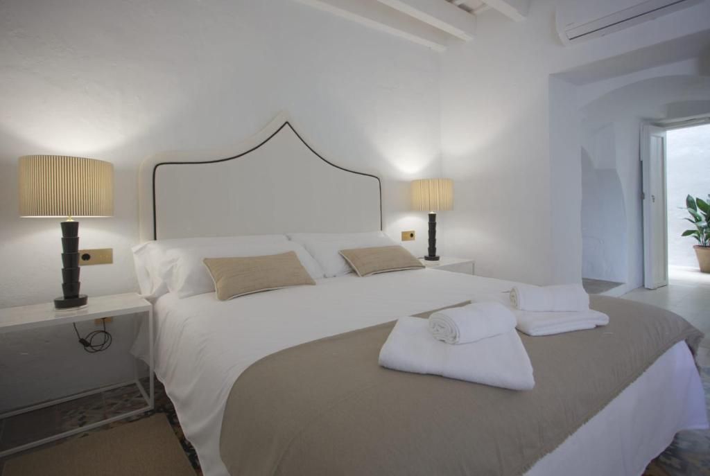 A neatly made bed with white linens and beige pillows, two bedside lamps, and a modern headboard.