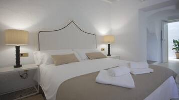 A neatly made bed with white linens and beige pillows, two bedside lamps, and a modern headboard.