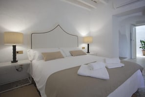 Una cama bien hecha con sábanas blancas y almohadones color beige, dos lámparas de noche y un cabecero moderno.