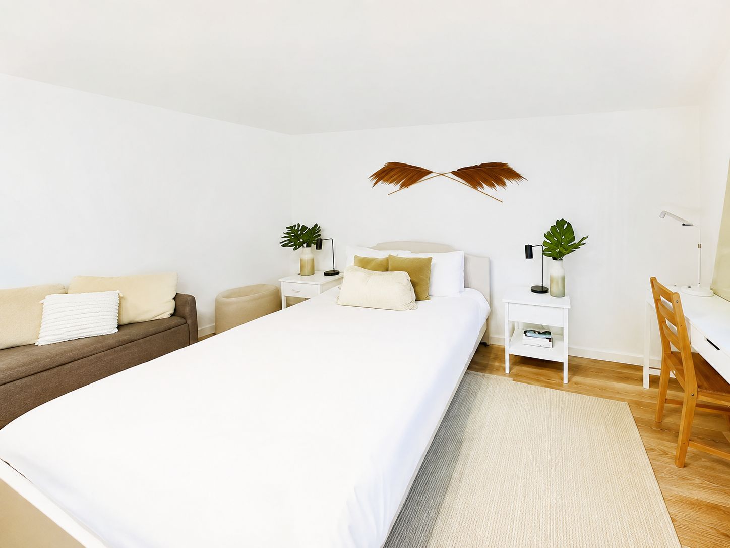 A modern bedroom with a large bed, a desk, a chair, and a small side table.