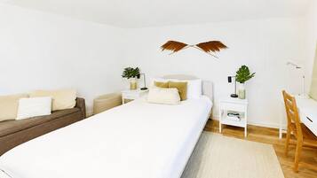 A modern bedroom with a large bed, a desk, a chair, and a small side table.