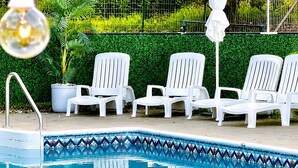 Une piscine dont le bord est recouvert de carrelage, entourée de chaises longues blanches et agrémentée d’une plante en pot.