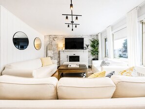Una sala de estar moderna con chimenea de ladrillo blanco, un televisor de pantalla plana montado encima y un amplio ventanal con vistas al exterior.