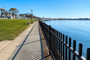 A waterfront promenade with a concrete walkway, benches, and a metal railing.