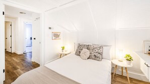 Une chambre à coucher avec un grand lit, deux tables de chevet avec des lampes, une petite table avec une plante et une carte accrochée au mur.
