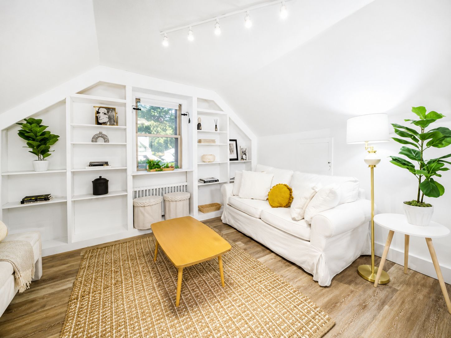 A modern living room with a white sofa, a yellow ottoman, and a round side table.