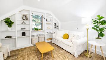 A modern living room with a white sofa, a yellow ottoman, and a round side table.