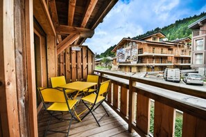 A wooden deck with yellow chairs and a table, overlooking a mountainous area with buildings. - 200m from ski slopes, 1st floor, balcony, ski locker, 30m², Les Gets (Les Gets)