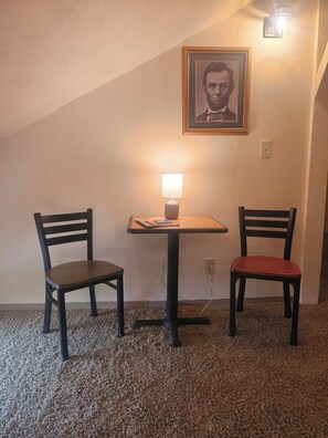 Una habitación con una mesa y dos sillas, un cuadro en la pared y una lámpara sobre la mesa.