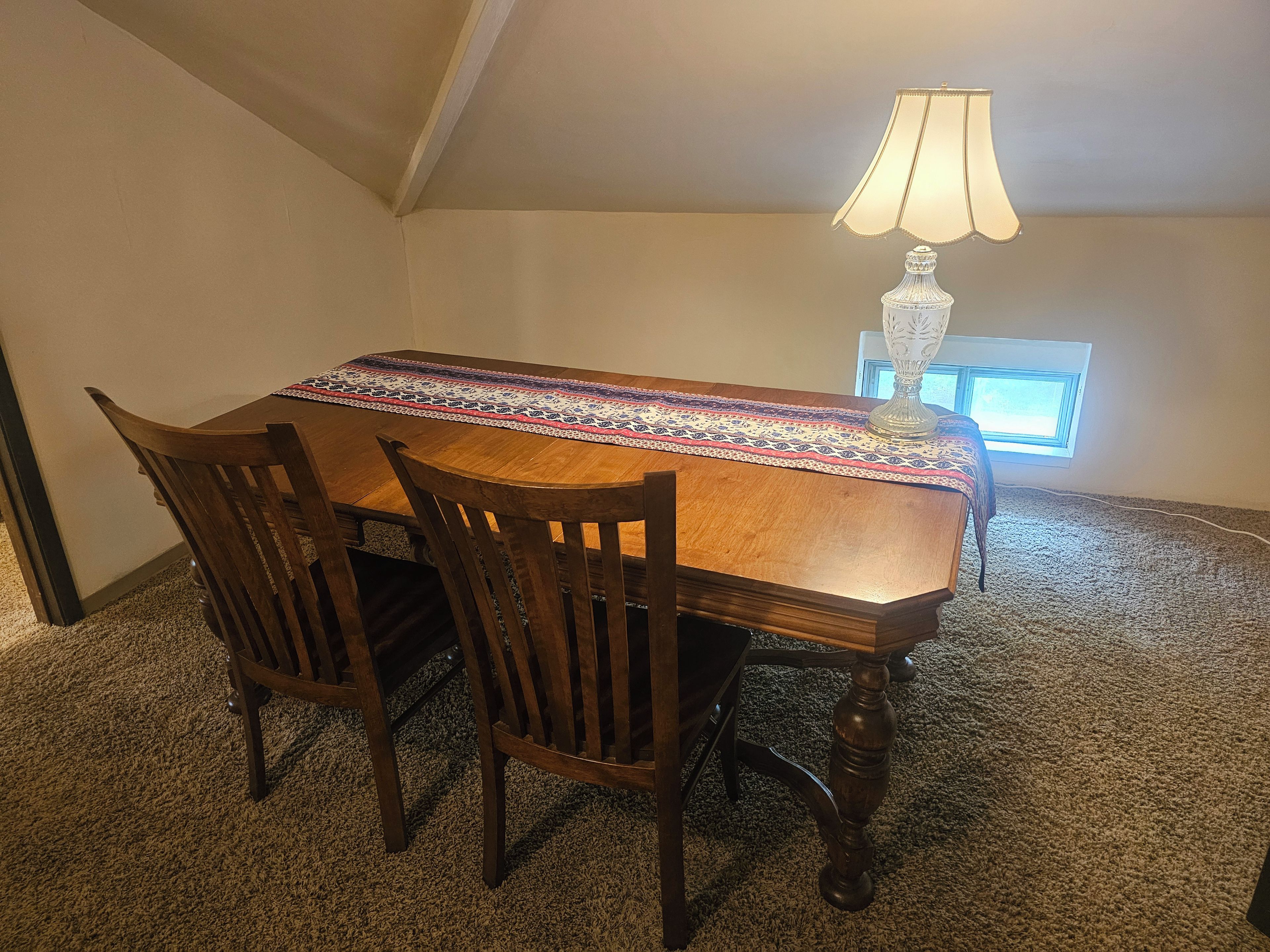 A dining area with a table, chairs, a lamp, and a carpeted floor.