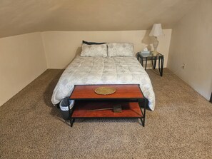 Un dormitorio con cama, mesita de noche, lámpara y un pequeño banco de madera.