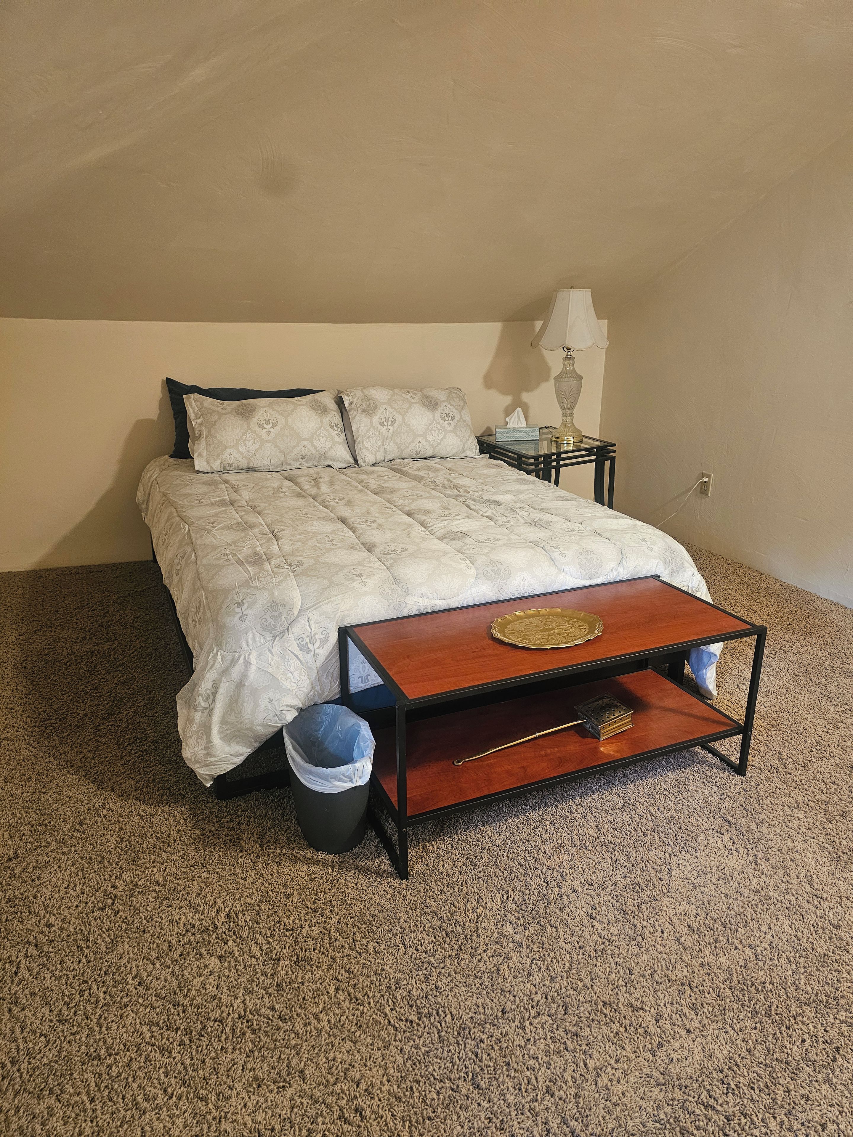 A bedroom with a bed, bedside table, lamp, and a small wooden table with a tray.