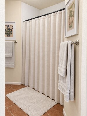 Ein Badezimmer mit Duschvorhang, einem Handtuchhalter mit Handtüchern, einem gerahmten Bild an der Wand und einem strukturierten Teppichboden.