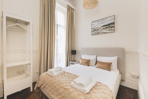 A hotel room with a bed, a wardrobe, a painting, and a window with curtains. - South Kensington Period Retreat (London)
