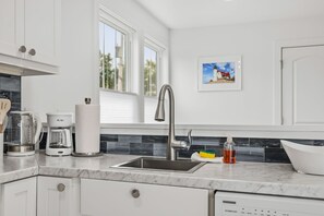A modern kitchen with a stainless steel sink, a coffee maker, and a dish soap bottle. - Lake Breeze | Hot Tub | Steps to Lake Michigan! (South Haven)