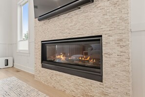 Ein moderner Kamin mit Steinverkleidung, darüber ein Flachbildfernseher und zur linken Seite ein Fenster.