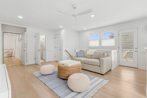 A modern living room with a sofa, ottomans, and a ceiling fan. - Lake Breeze | Hot Tub | Steps to Lake Michigan! (South Haven)