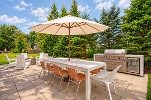 Eine Terrasse im Freien mit Tisch, Stühlen, Sonnenschirm und Grill.