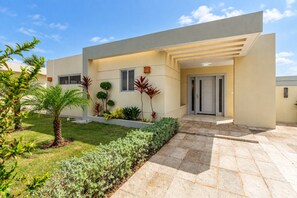 Ein modernes, zweistöckiges Haus mit Flachdach, einer Veranda und einem gepflegten Rasen mit verschiedenen Pflanzen.