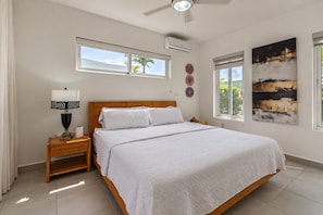 Quarto com cama, mesa de cabeceira, luminária e obra de arte.