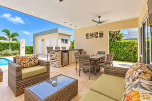 Ein möblierter Außenbereich mit Korbmöbeln, einem Tisch mit Glasplatte und einem Pool im Hintergrund.