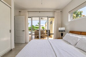 Ein Schlafzimmer mit einem großen Bett, einem Nachttisch, einer Lampe und Blick auf eine Terrasse mit Tisch und Stühlen.
