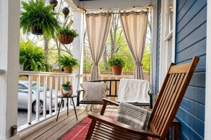A porch with a wooden swing chair, a small table with a potted plant, and a hanging planter with greenery. - East Austin Gem, Cowboy Pool, Yard Games, Golf Put (Austin)