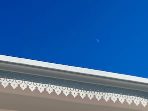 Kirkkaan sininen taivas, jossa näkyy sirpinmuotoinen kuu, ja rakennuksen reunassa valkoinen koristeellinen reunalista.