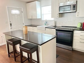 A kitchen with a central island, two bar stools, a microwave, an oven, and a window.