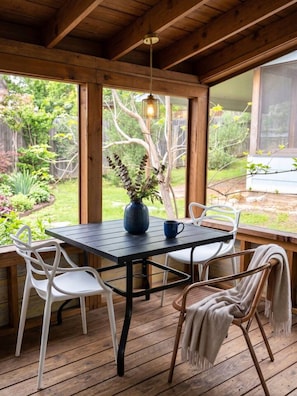 An outdoor wooden deck with a table and chairs, a hanging light fixture, and a view of a garden. - King, Heart of East Austin, Walkable, Home Office (Austin)