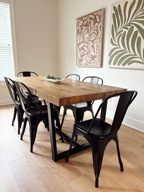 A dining table with six chairs, a bowl of greens, and two abstract wall art pieces. - The Townhouse on Encore (Cookeville)