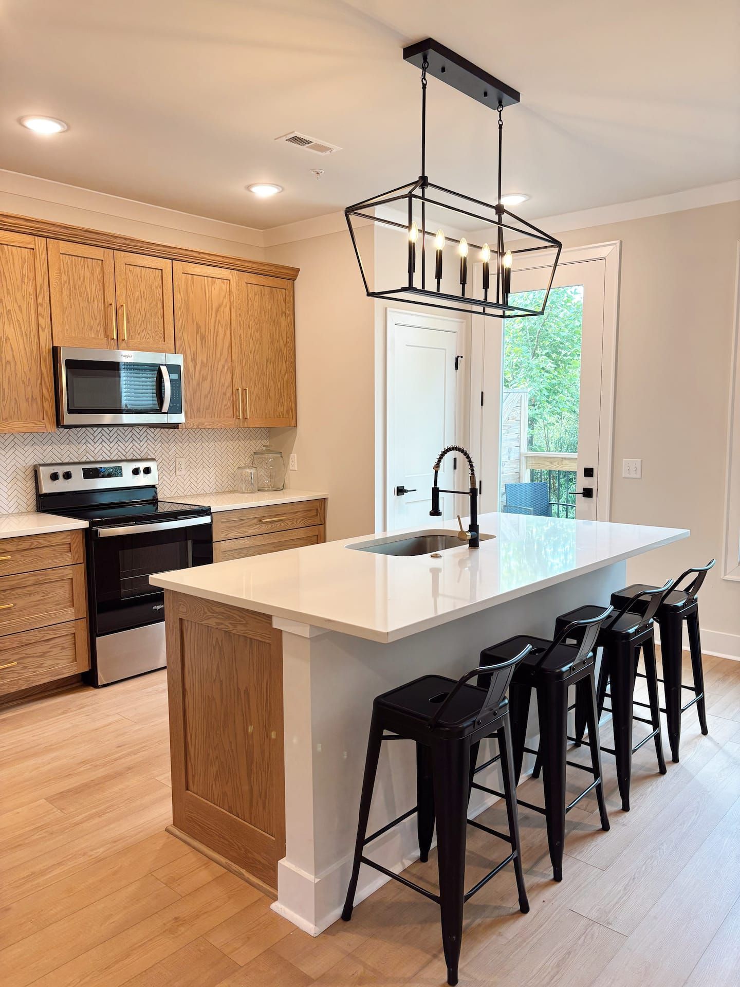 A modern kitchen with wooden cabinets, stainless steel appliances, a large island with bar stools, and a pendant light.