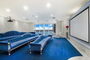 A room with a large screen, a blue sofa set, and a view of the sky through the windows. - Spectacular 46th Floor Corner 2BR Bay & City View (Miami)