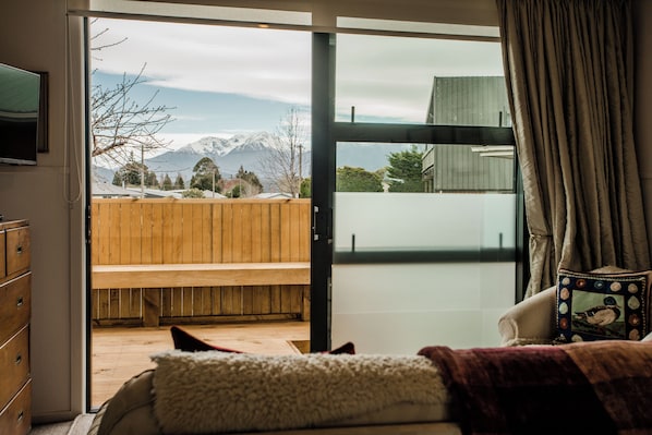 A bedroom with a bed, a wooden bench, and a view of mountains through a sliding glass door.