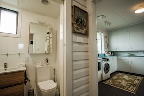 Ein kleines Badezimmer mit Toilette, Waschbecken und Spiegel. Daneben befindet sich ein Waschbereich mit Waschmaschine und Wäscheständer.