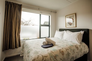Ein Hotelzimmer mit Bett, einem fensterbelaubten Fenster, einem gerahmten Bild an der Wand und Teppichboden.