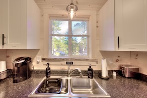 Una cocina con un lavamanos doble, una cafetera y una ventana con persianas.
