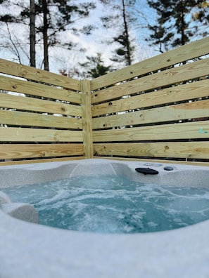 Eine Holzterrasse umgibt eine Hot Tub mit Steinrand.
