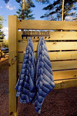 Un banc en bois avec une pancarte indiquant « HEURE DE DÉTENTE DANS LE JACUZZI » et deux serviettes bleues suspendues à un crochet.