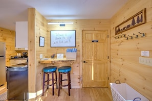 A cabin interior with a kitchenette, two stools, a door labeled 'Mechanical Room,' and a welcome sign. - Ubuntu Haus • Near Castle Rock Lake • HOT TUB! (Friendship)