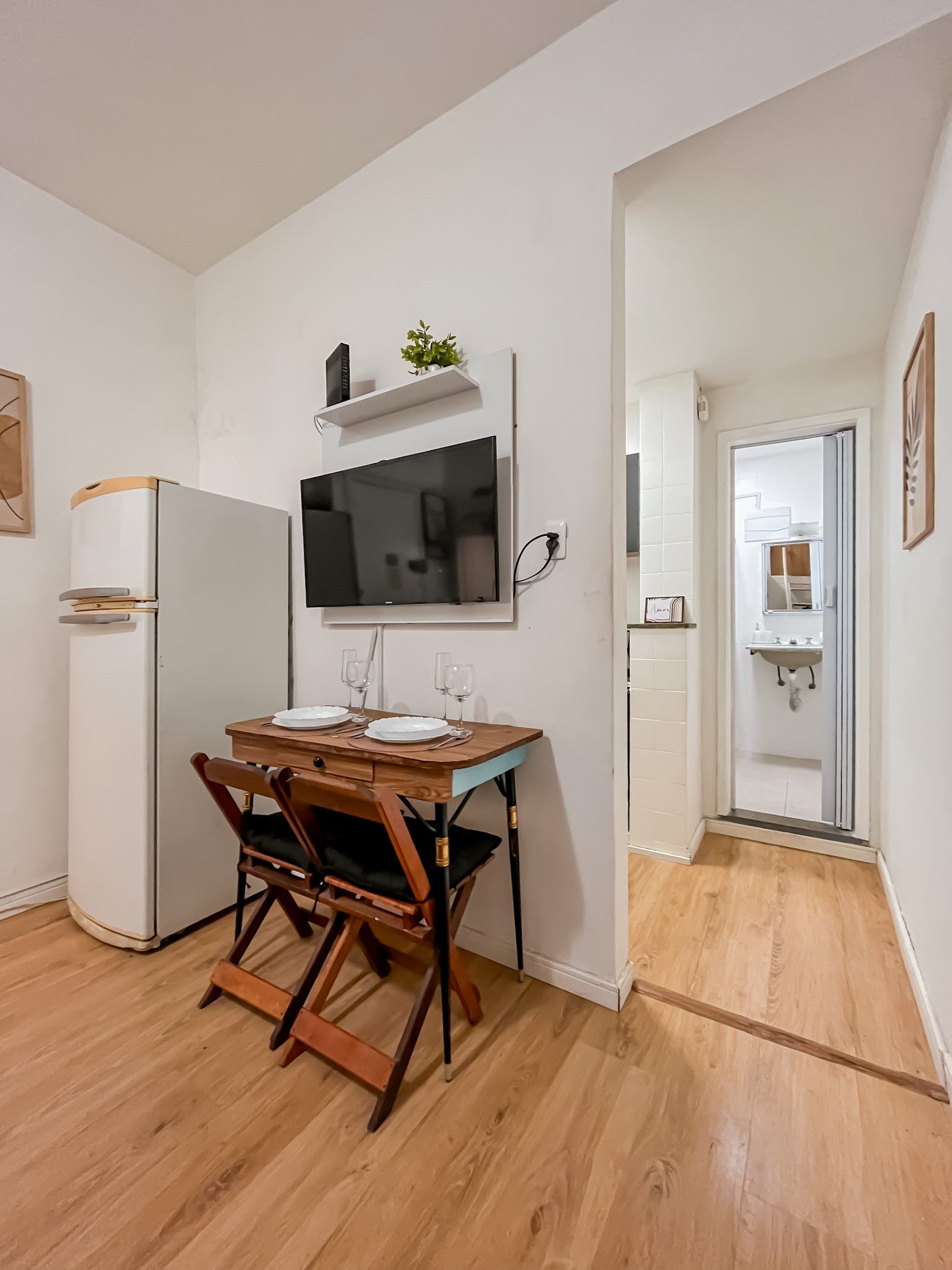 A compact kitchen with a dining table, chairs, a TV, and a refrigerator.
