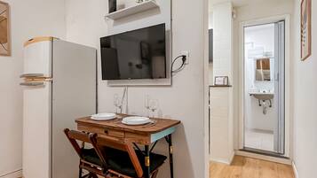 A compact kitchen with a dining table, chairs, a TV, and a refrigerator.