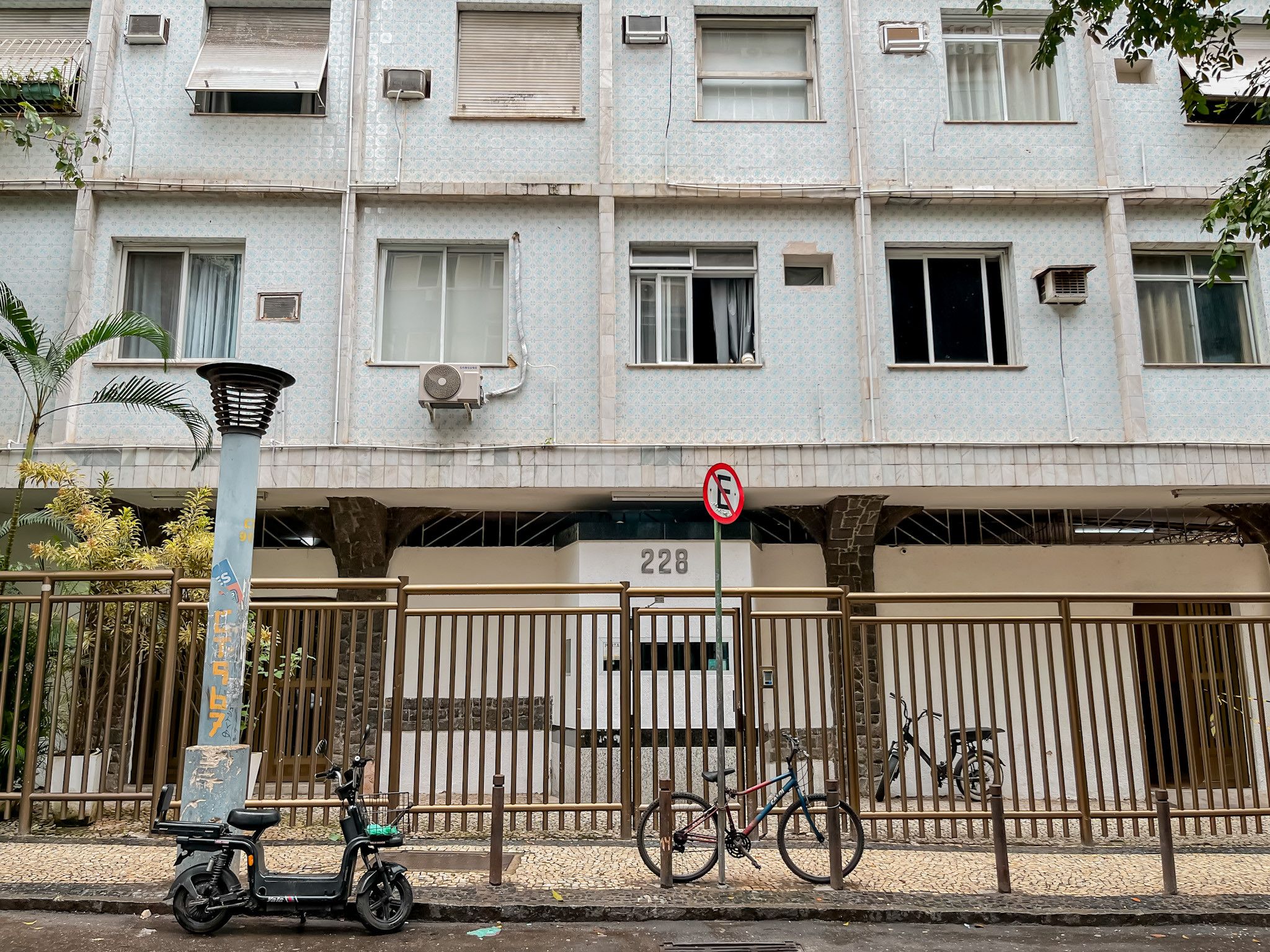 A multi-story residential building with a gated entrance, numbered 228, and a no-parking sign.